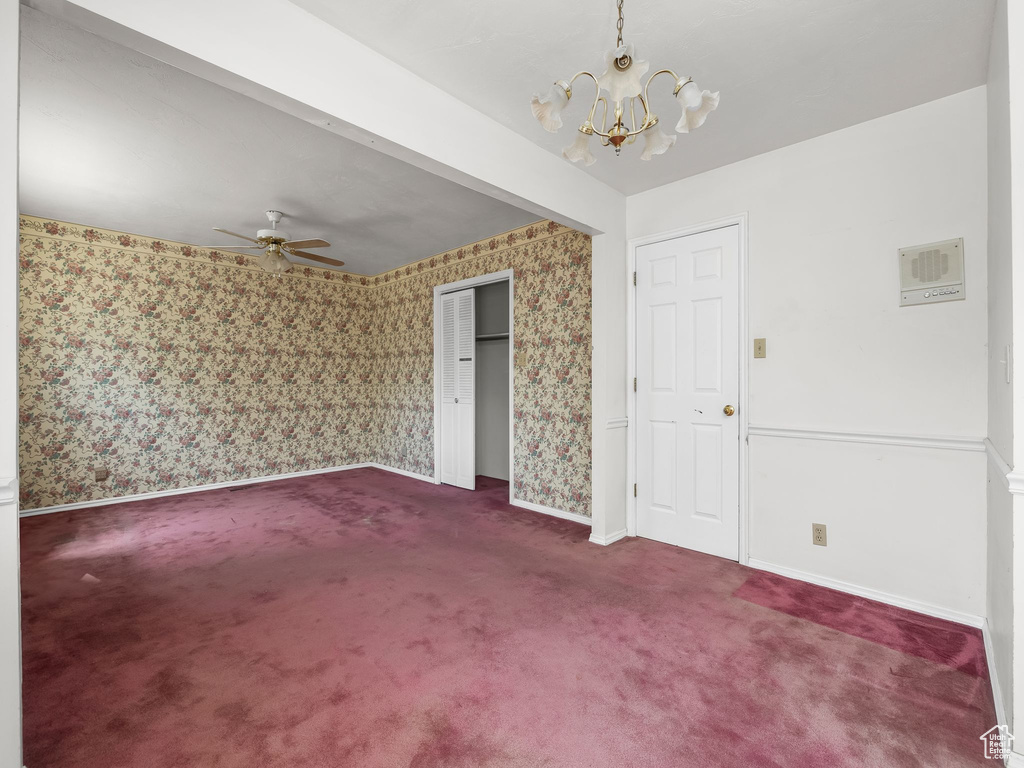 Unfurnished room featuring wallpapered walls, dark carpet, a ceiling fan, and a chandelier