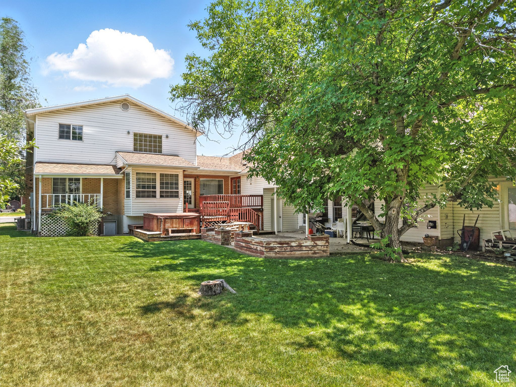 Rear view of property featuring a hot tub, a yard, brick siding, and a patio