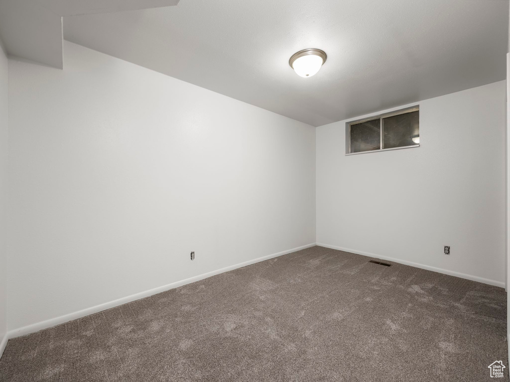 Spare room featuring dark colored carpet and baseboards