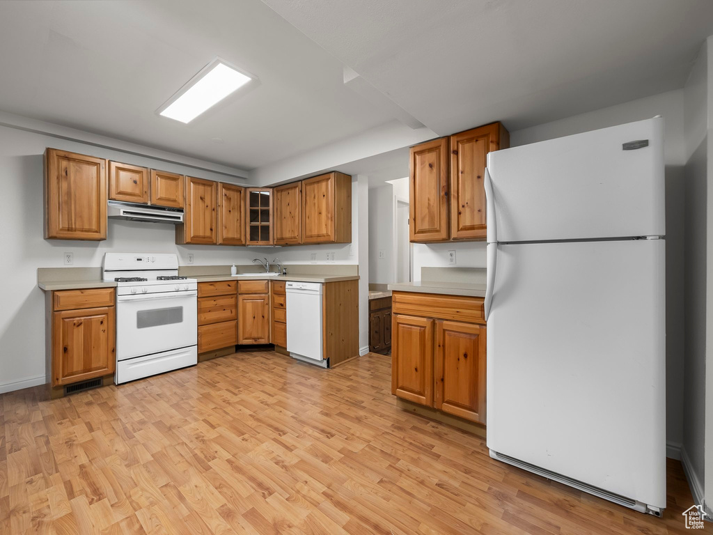 Kitchen featuring white appliances, range hood, light wood-style floors, and light countertops