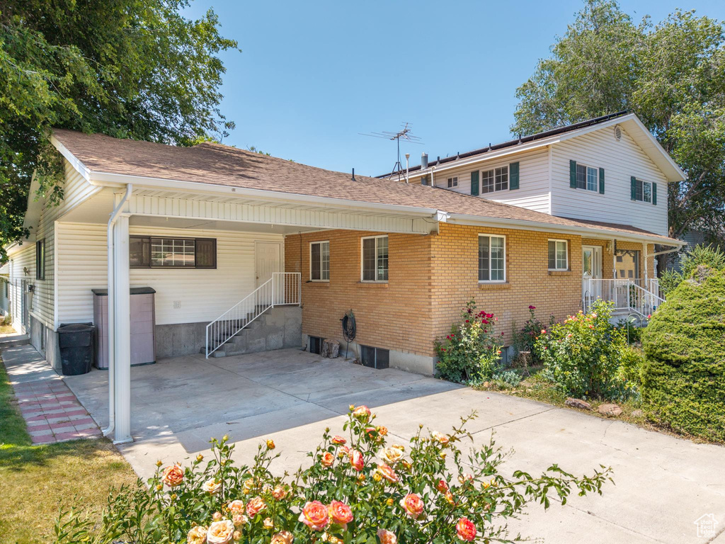 Rear view of property with an attached carport, brick siding, roof with shingles, and concrete driveway