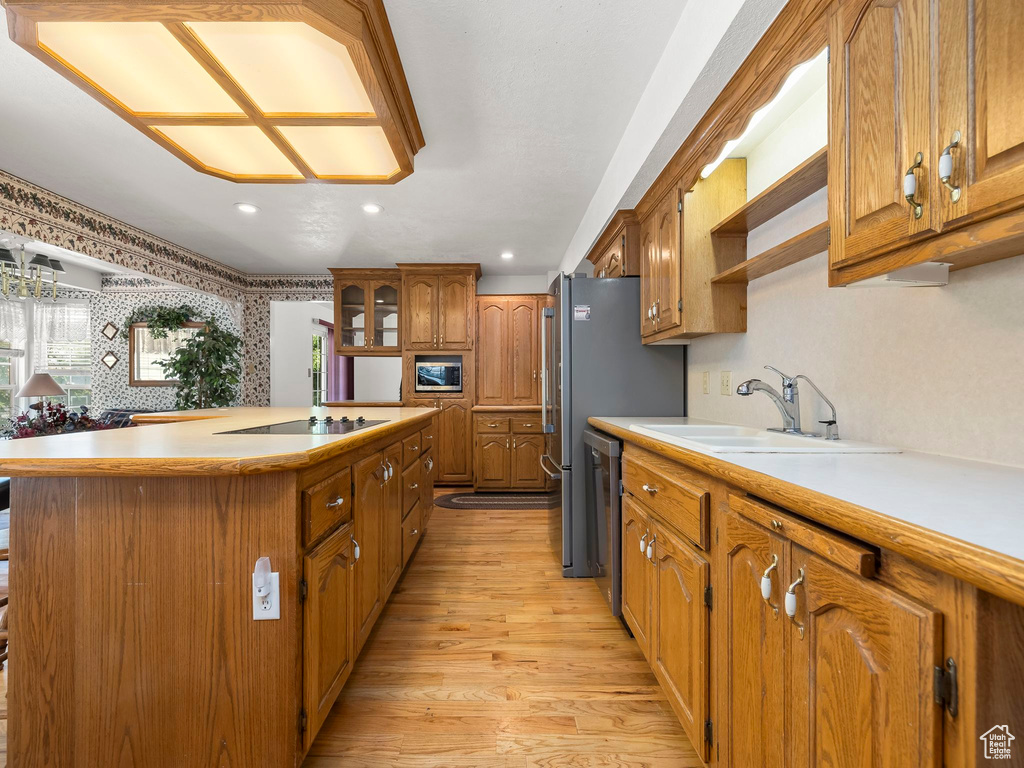 Kitchen with a center island, appliances with stainless steel finishes, light wood-style floors, brown cabinetry, and light countertops