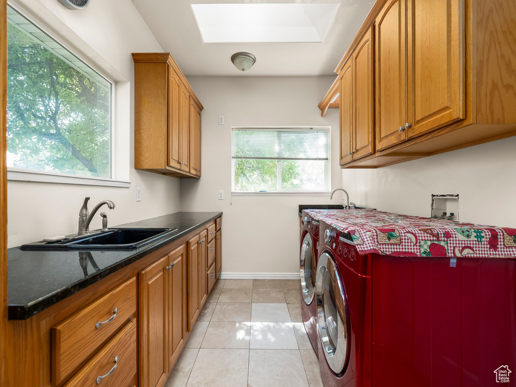 Washroom with a skylight, cabinet space, independent washer and dryer, and light tile patterned floors