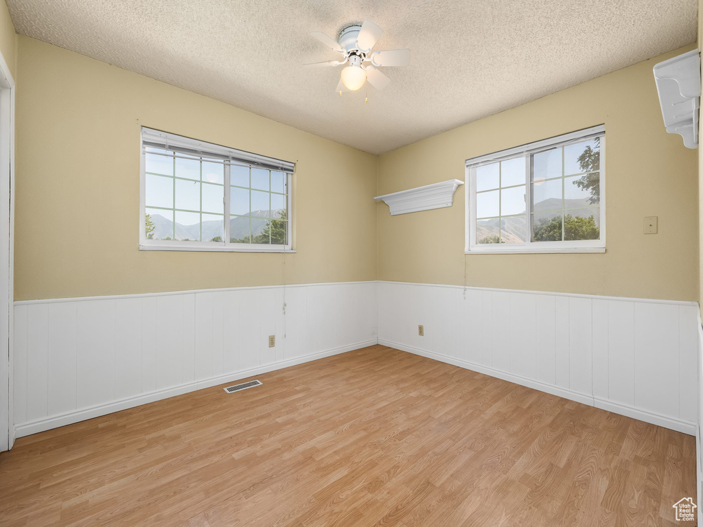 Spare room featuring light wood-style flooring, healthy amount of natural light, a textured ceiling, a wainscoted wall, and ceiling fan