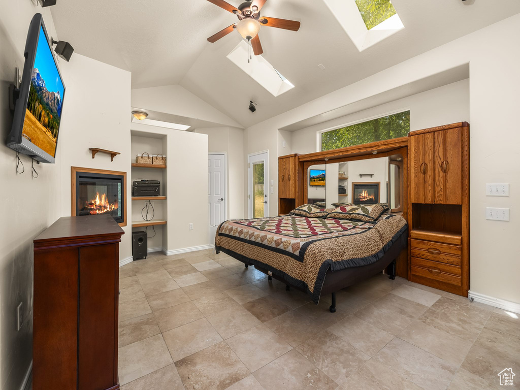 Bedroom featuring a glass covered fireplace, a skylight, ceiling fan, and high vaulted ceiling