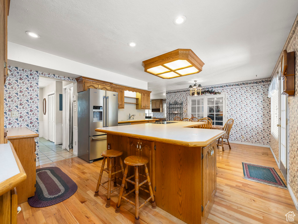 Kitchen featuring high end refrigerator, wallpapered walls, light wood-style floors, a kitchen island, and light countertops