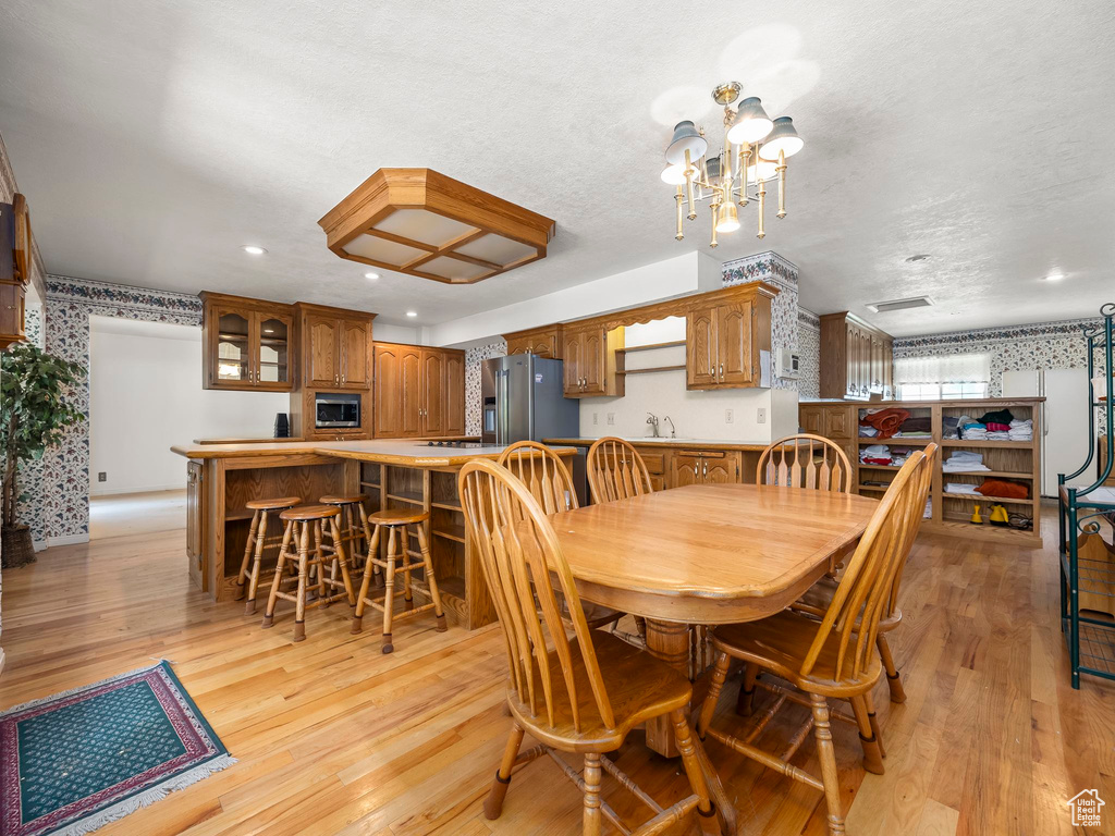 Dining space with light wood finished floors, a chandelier, recessed lighting, wallpapered walls, and a textured ceiling
