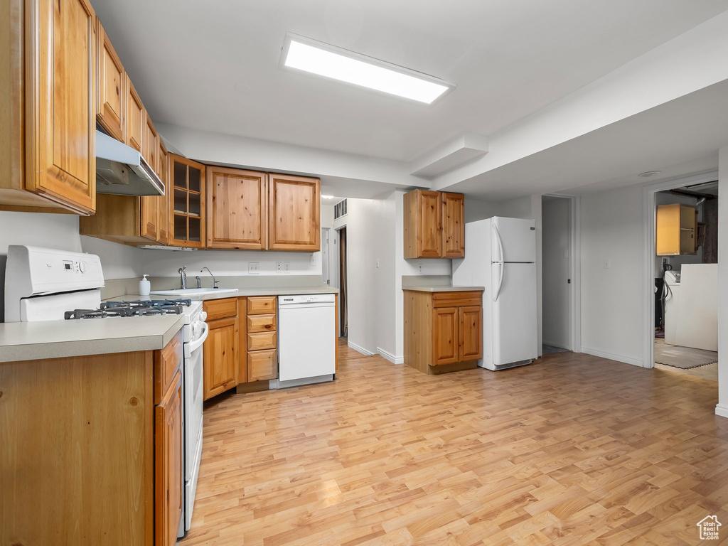 Kitchen with white appliances, under cabinet range hood, light wood-style flooring, and light countertops