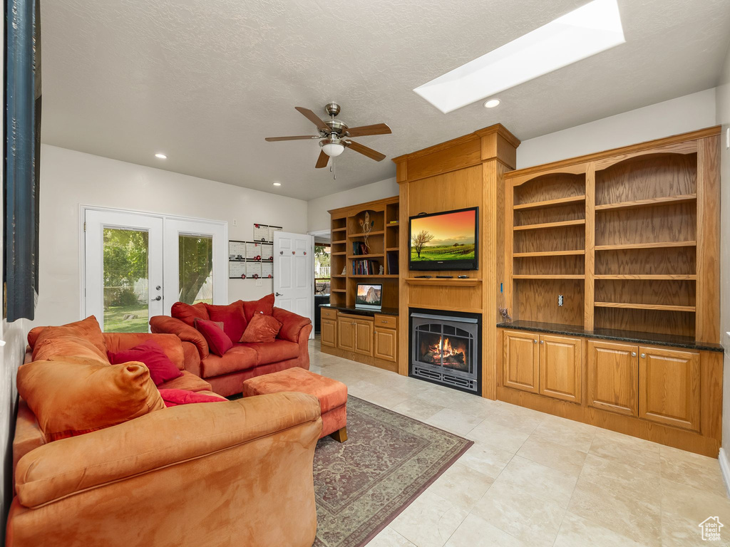 Living room featuring a fireplace, a ceiling fan, recessed lighting, french doors, and a skylight
