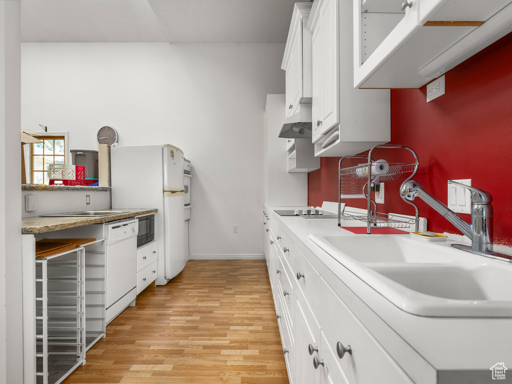 Kitchen with white appliances, light wood-style flooring, under cabinet range hood, white cabinetry, and light countertops