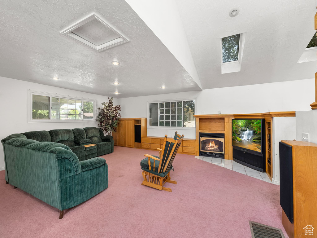 Carpeted living room with a fireplace with flush hearth, a textured ceiling, recessed lighting, and a skylight