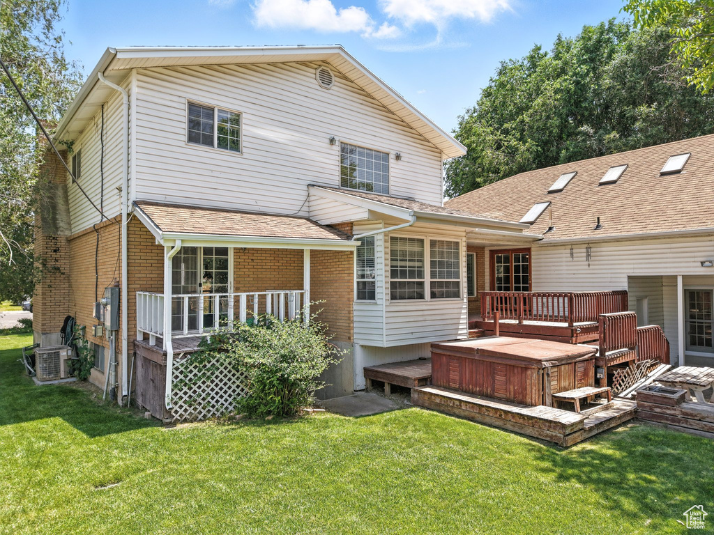 Rear view of property featuring a hot tub, a deck, a yard, and brick siding