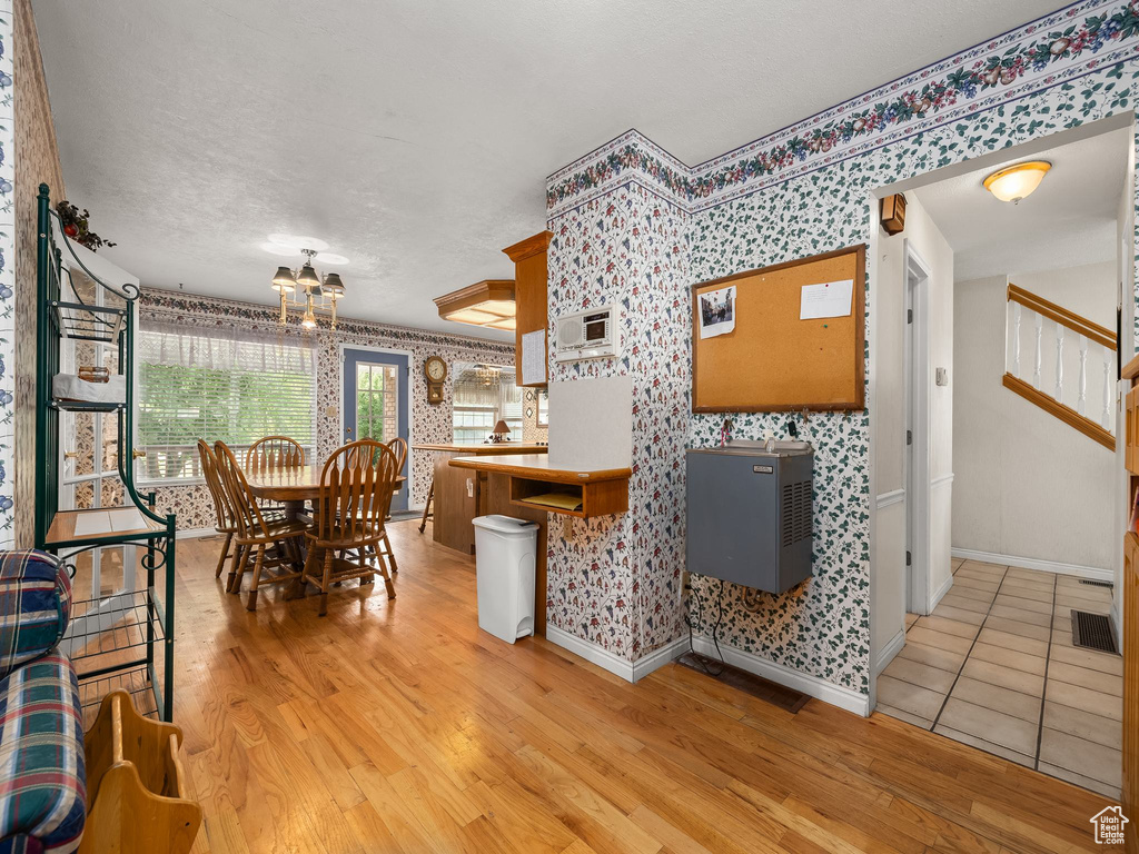 Dining space featuring wallpapered walls, light wood finished floors, a chandelier, stairway, and a textured ceiling