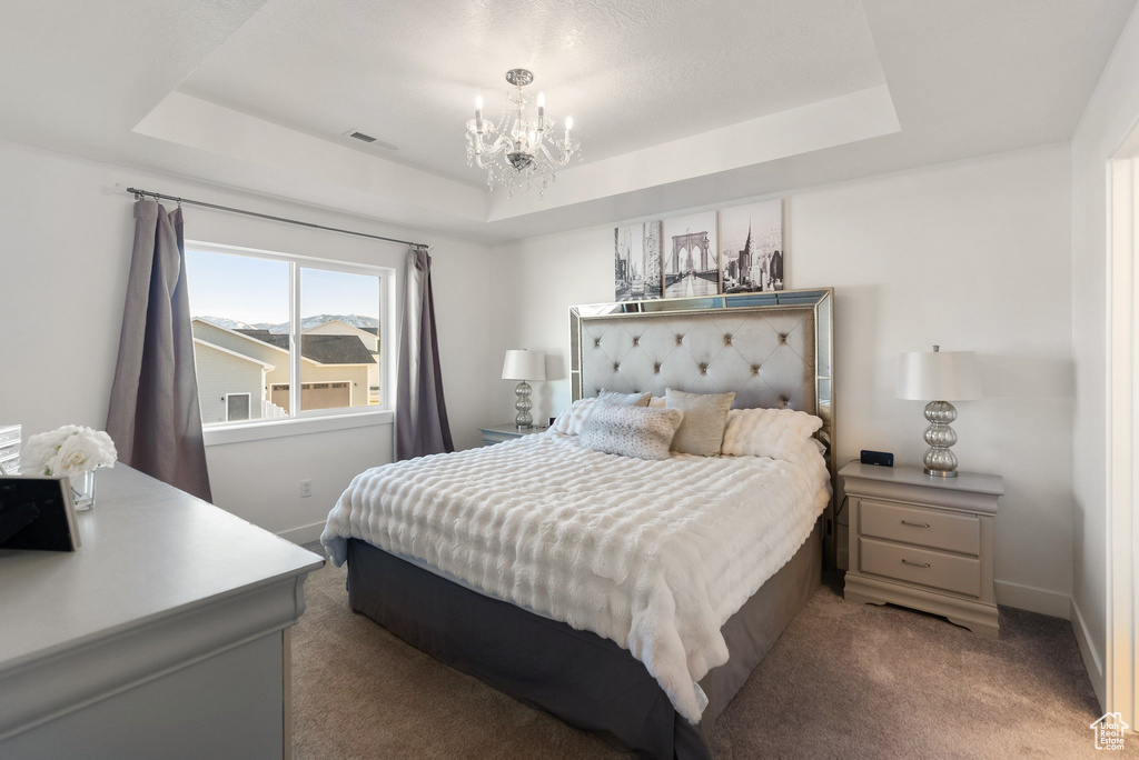 Bedroom with a tray ceiling, a chandelier, and carpet