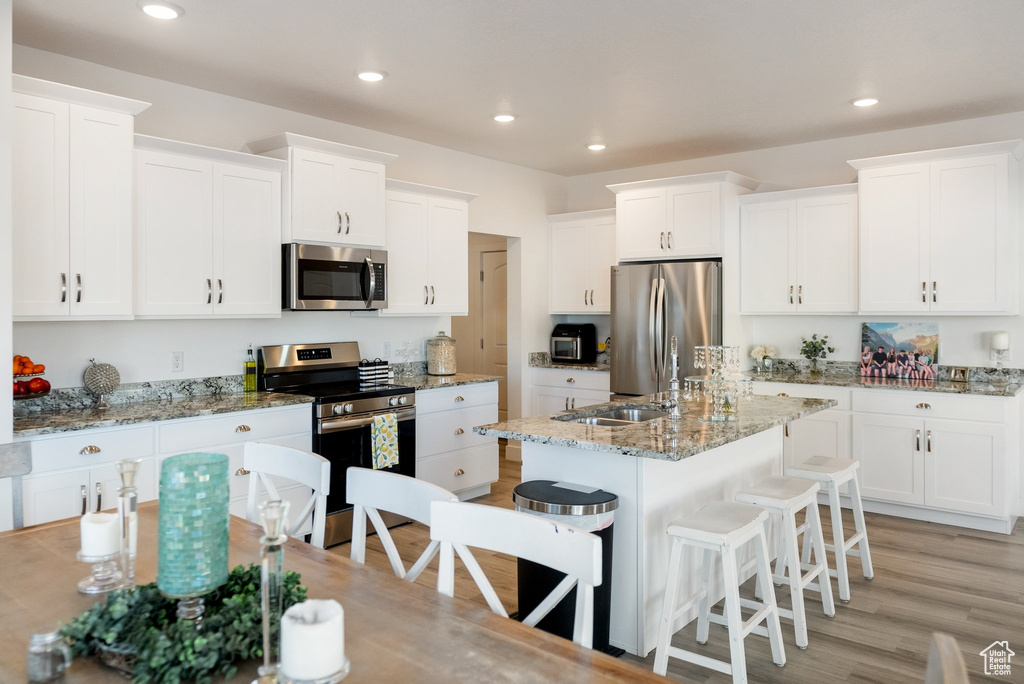Kitchen featuring appliances with stainless steel finishes, a breakfast bar, white cabinets, and recessed lighting