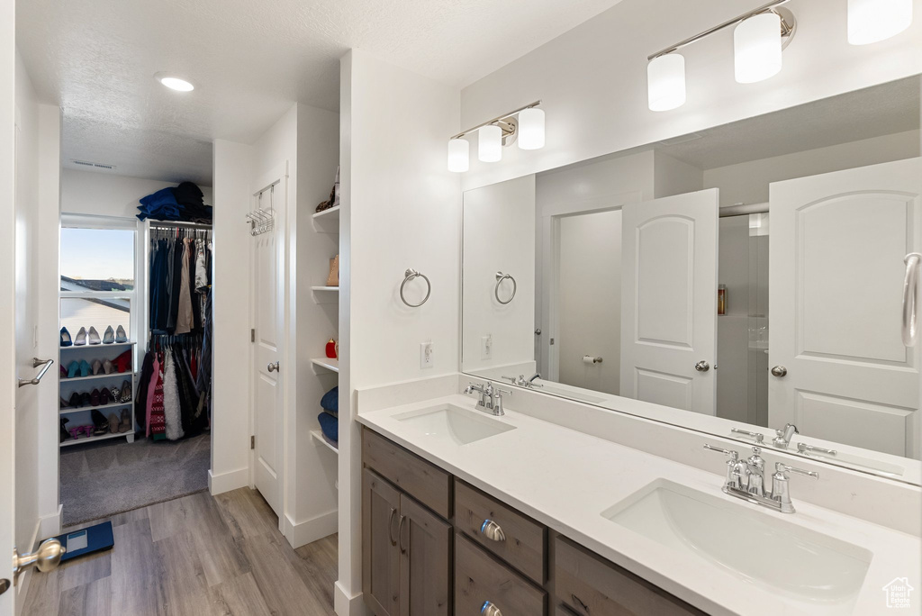 Full bath featuring wood finished floors, double vanity, a walk in closet, an enclosed shower, and a textured ceiling