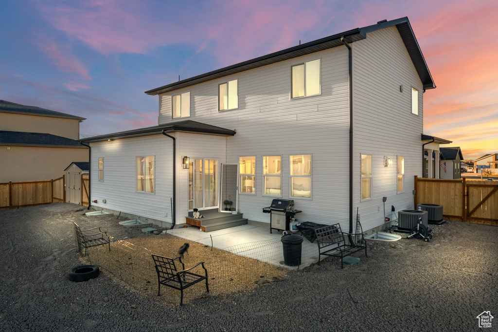 Back of house at dusk featuring a storage unit, a fenced backyard, and a patio
