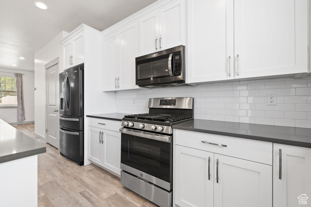 Kitchen featuring appliances with stainless steel finishes, dark countertops, recessed lighting, white cabinets, and light wood finished floors
