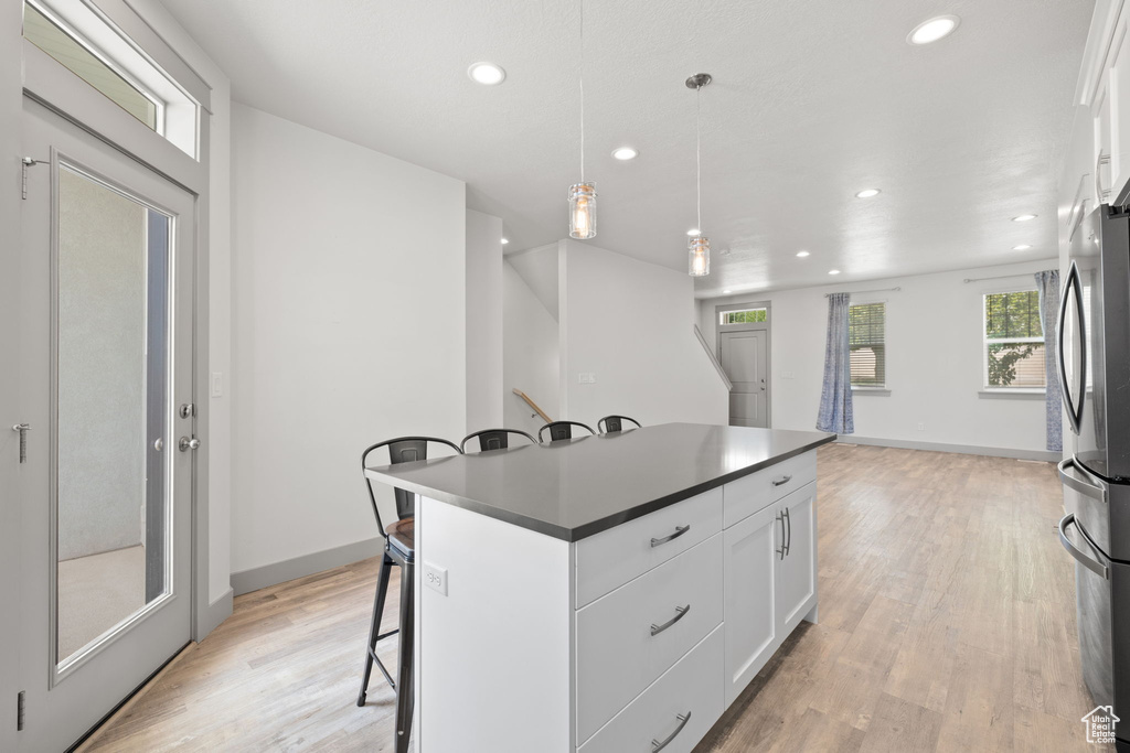 Kitchen with freestanding refrigerator, a kitchen bar, recessed lighting, light wood-style flooring, and white cabinetry
