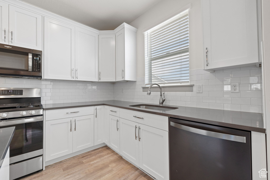 Kitchen with stainless steel appliances, dark countertops, white cabinetry, and tasteful backsplash
