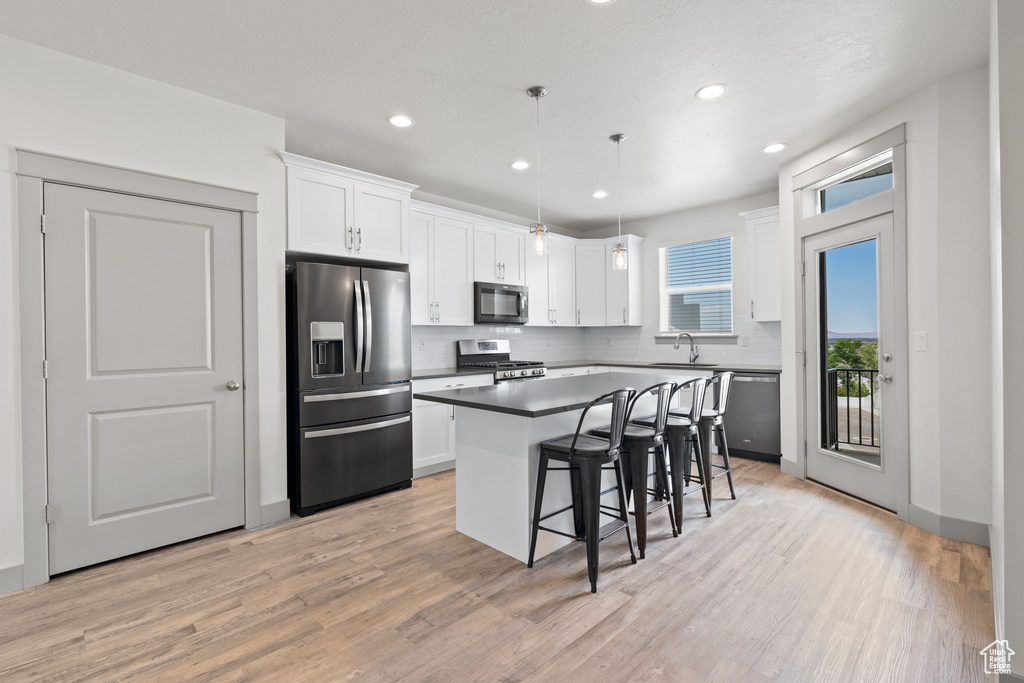 Kitchen with appliances with stainless steel finishes, a kitchen breakfast bar, white cabinetry, decorative backsplash, and recessed lighting