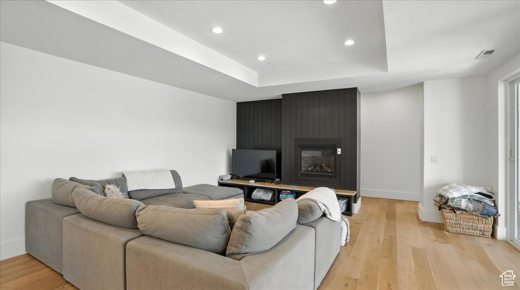 Living room with light wood-style floors, recessed lighting, a large fireplace, and a tray ceiling