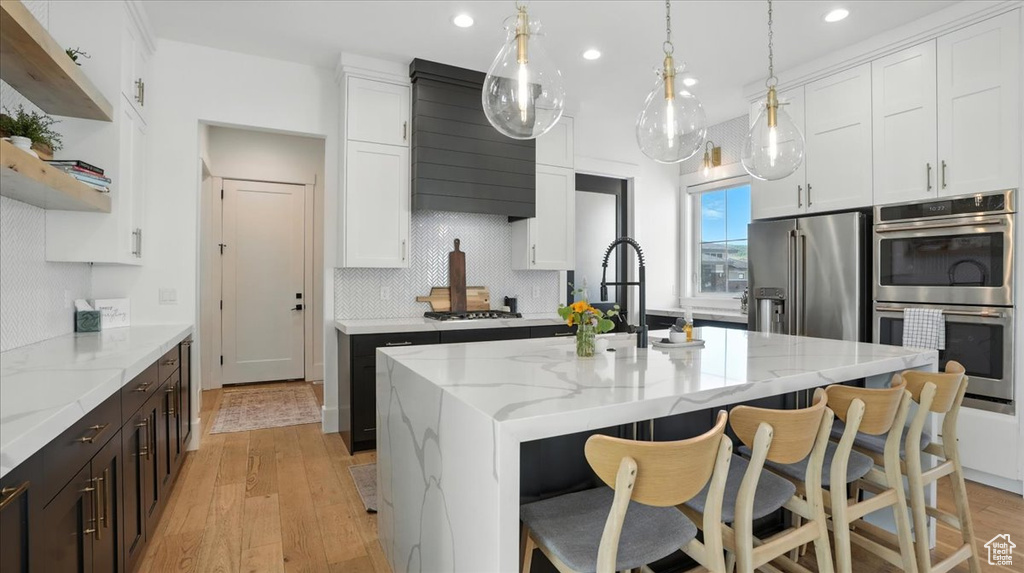 Kitchen with appliances with stainless steel finishes, exhaust hood, light wood-style floors, white cabinets, and recessed lighting