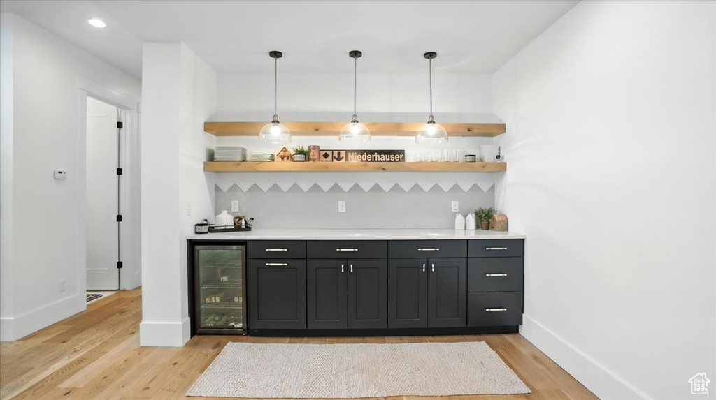 Indoor wet bar featuring wine cooler, light wood-style flooring, backsplash, and decorative light fixtures
