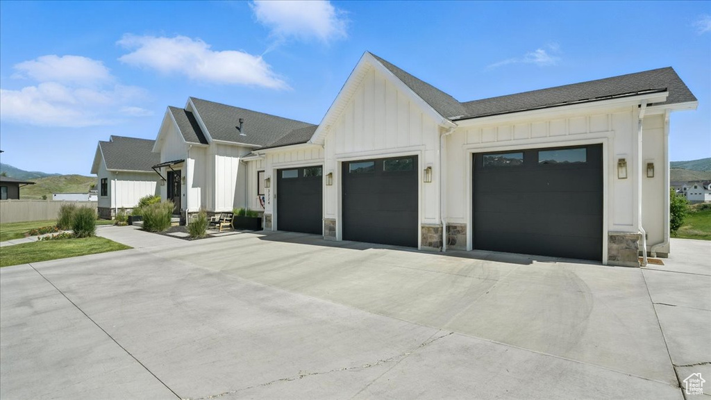 View of front of property with board and batten siding, a garage, stone siding, and concrete driveway