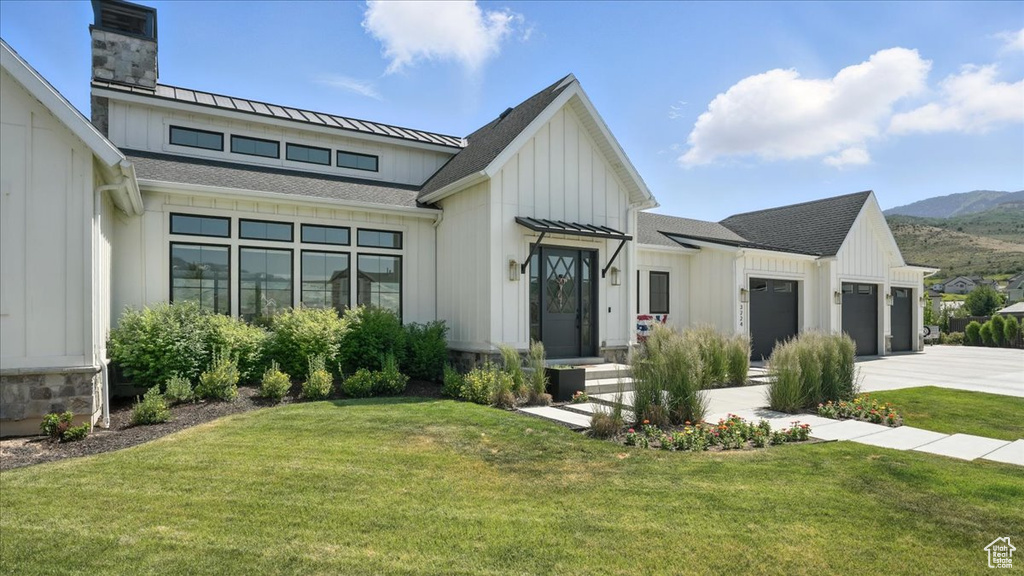 Modern farmhouse style home featuring an attached garage, driveway, board and batten siding, a front lawn, and a chimney
