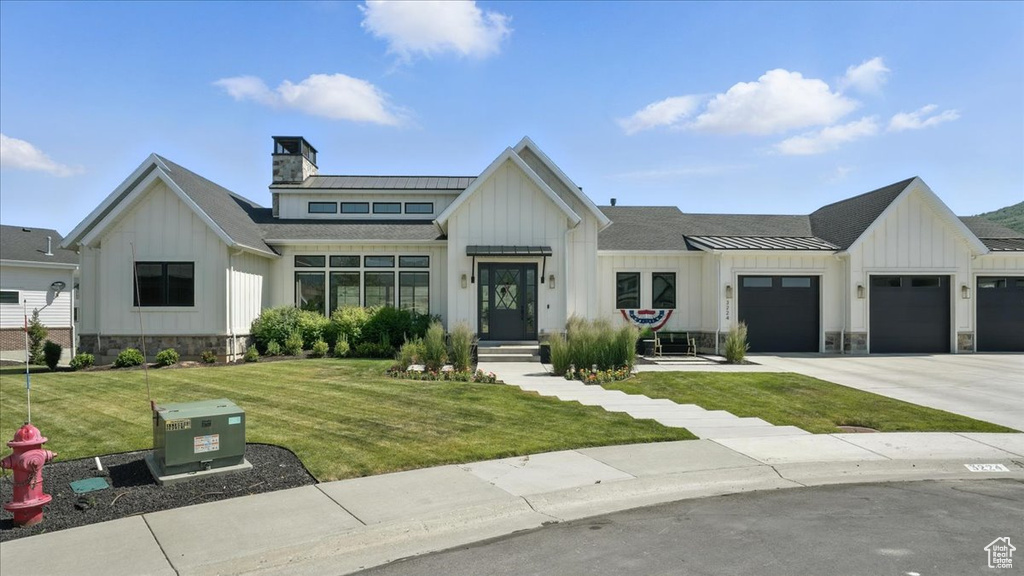 Modern farmhouse style home featuring board and batten siding, a garage, a front yard, and driveway