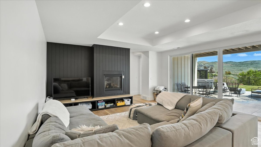 Living room with recessed lighting, light wood-style floors, a large fireplace, and a raised ceiling