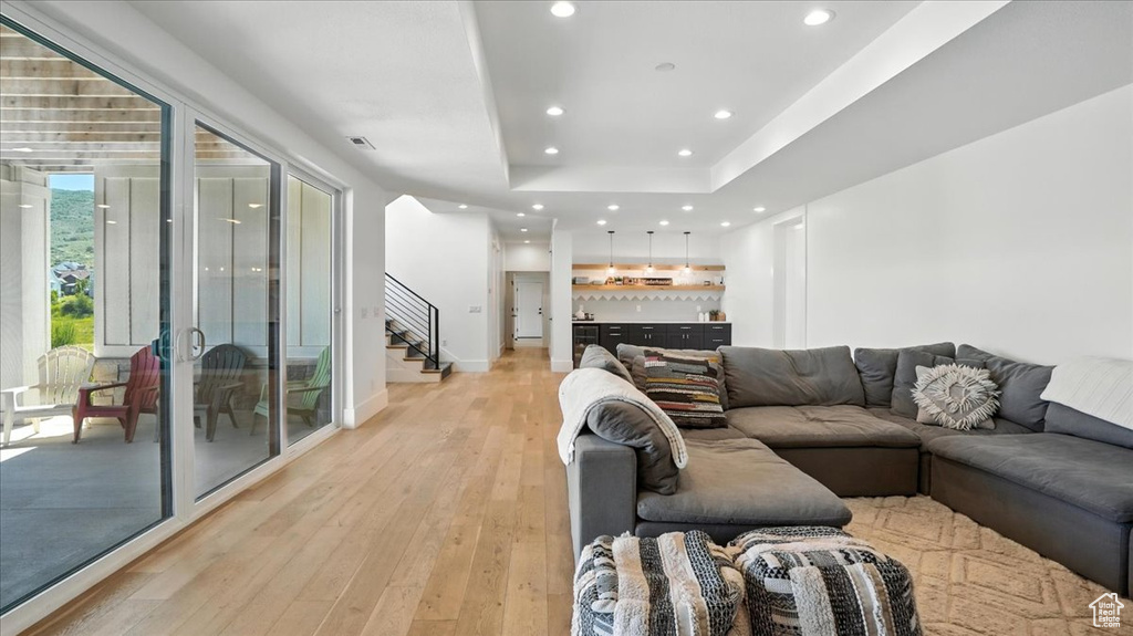 Living area featuring stairs, light wood-style flooring, recessed lighting, and a raised ceiling