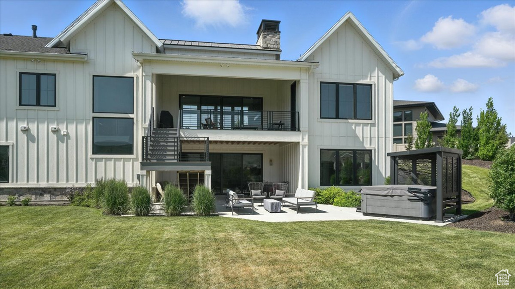 Back of property featuring board and batten siding, a balcony, outdoor lounge area, and a patio