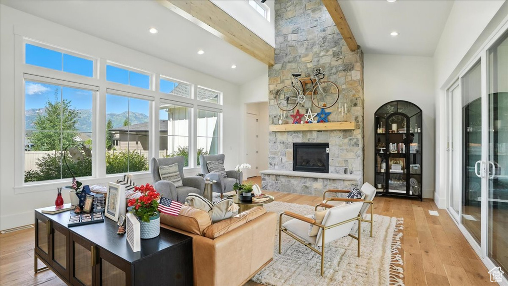 Living room featuring beamed ceiling, a stone fireplace, light wood-type flooring, high vaulted ceiling, and recessed lighting