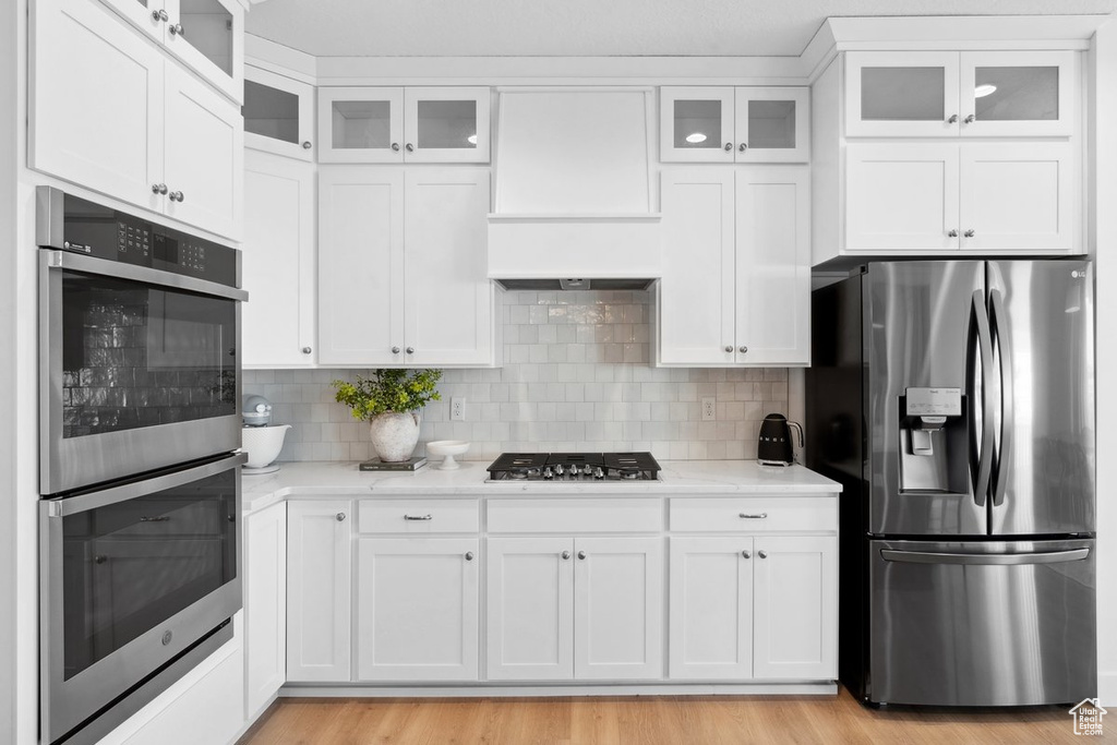 Kitchen with appliances with stainless steel finishes, white cabinetry, tasteful backsplash, and light wood finished floors