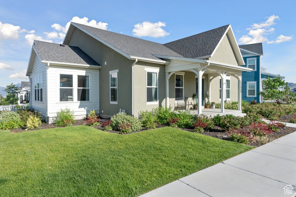 View of front of home with a porch, a front yard, roof with shingles, and stucco siding