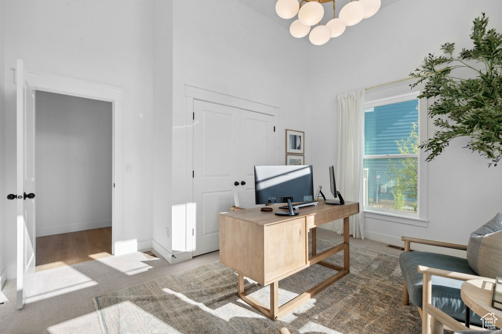 Office area featuring a towering ceiling, light carpet, and a chandelier