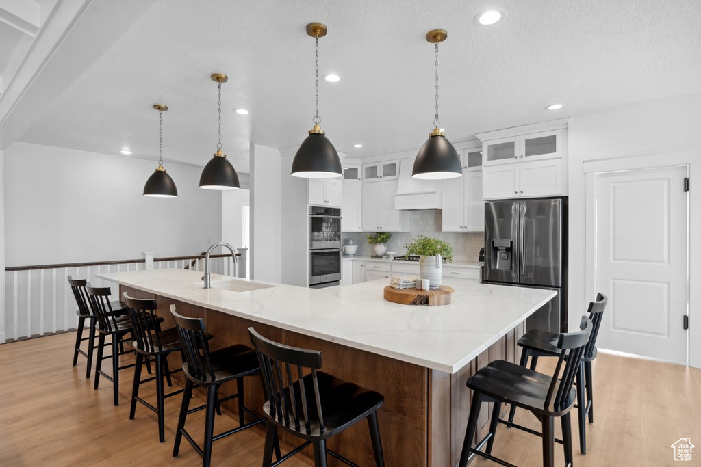 Kitchen featuring appliances with stainless steel finishes, light wood finished floors, a spacious island, white cabinetry, and recessed lighting