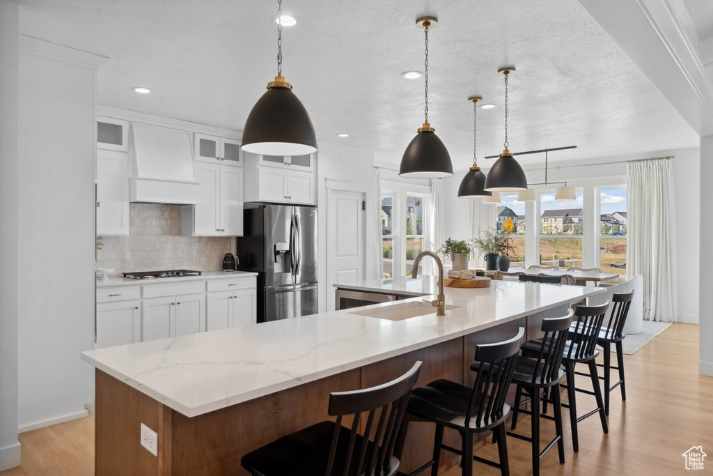 Kitchen with stainless steel fridge with ice dispenser, custom exhaust hood, gas cooktop, decorative backsplash, and a large island with sink