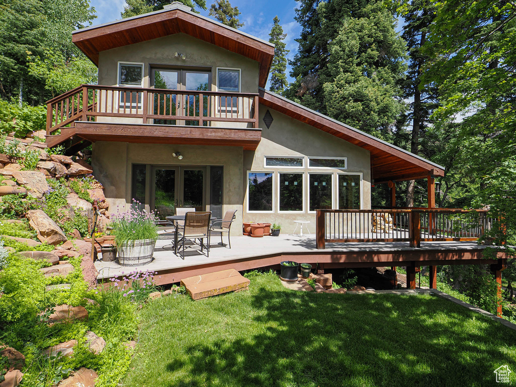 Back of house with a deck, stucco siding, and a lawn