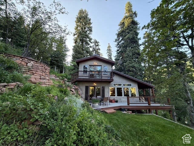 Rear view of house with a wooden deck, stucco siding, a yard, and a balcony