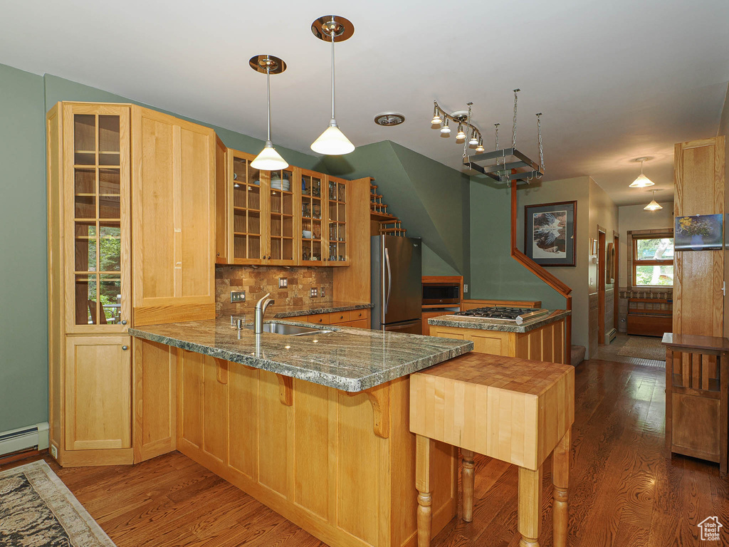 Kitchen with stainless steel appliances, wood finished floors, backsplash, a peninsula, and glass insert cabinets
