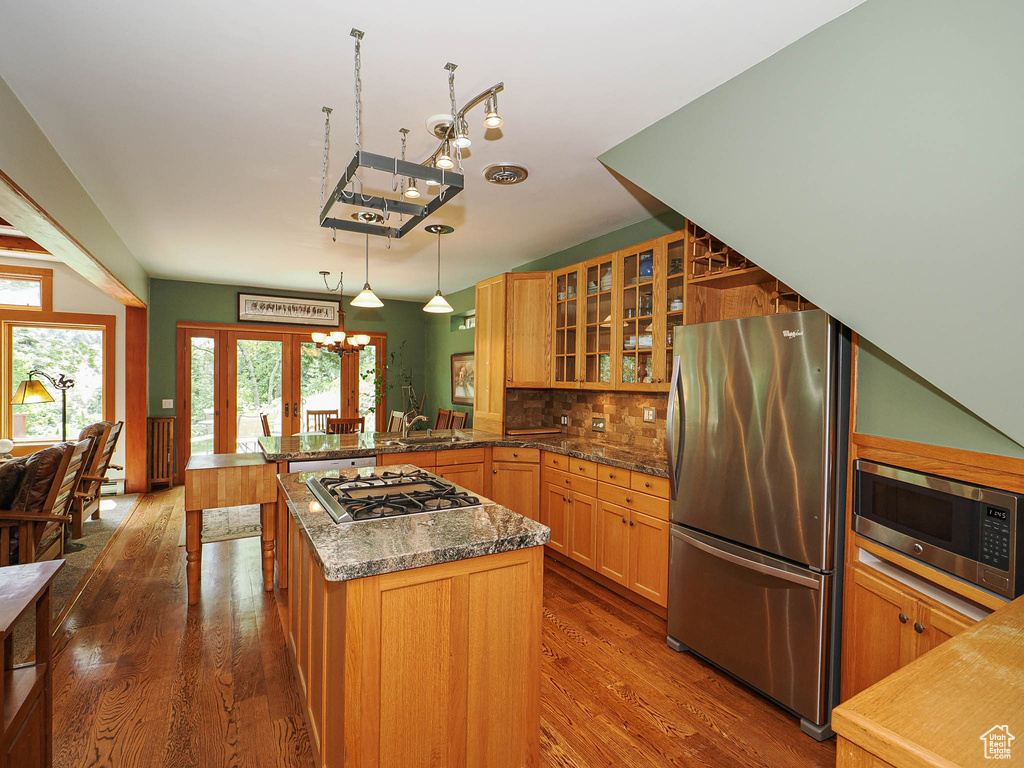 Kitchen featuring stainless steel appliances, a chandelier, a peninsula, dark wood-type flooring, and glass insert cabinets