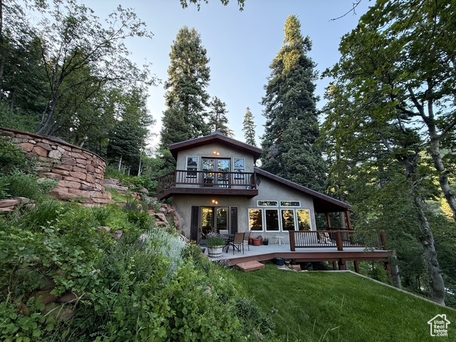 Rear view of property featuring stucco siding, a deck, a lawn, and a balcony