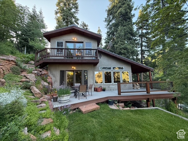 Rear view of house with stucco siding, a lawn, and a wooden deck