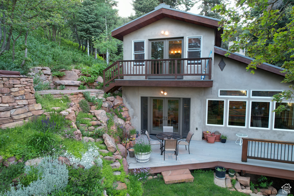 Rear view of house featuring french doors, stucco siding, a wooden deck, and a balcony