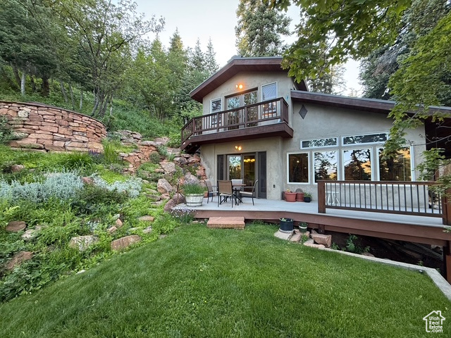 Rear view of house with stucco siding, a balcony, a lawn, and a wooden deck