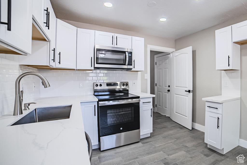 Kitchen with appliances with stainless steel finishes, white cabinets, light stone countertops, tasteful backsplash, and light wood-style flooring