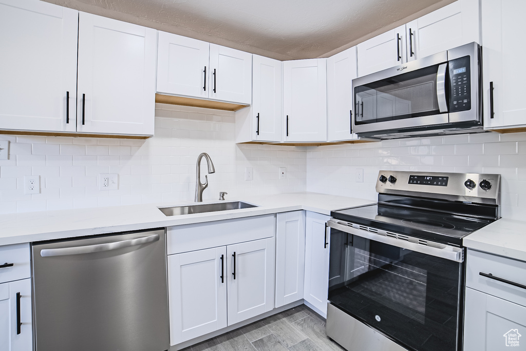 Kitchen with stainless steel appliances, light countertops, light wood-style flooring, and white cabinetry